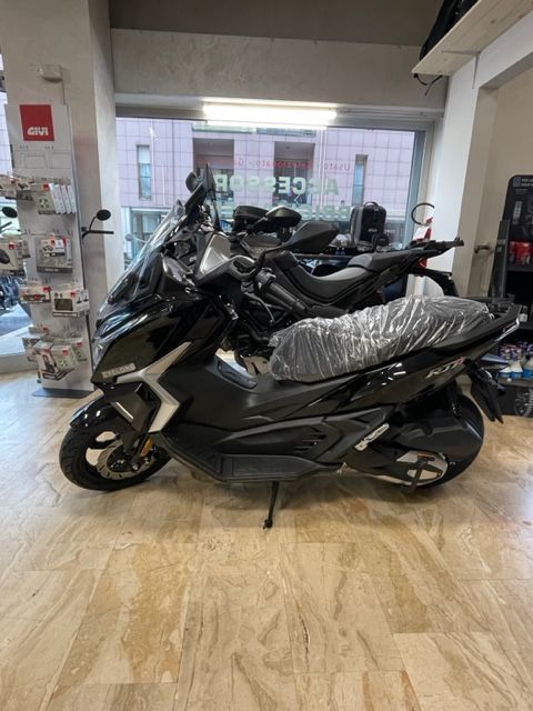 Uno scooter nero parcheggiato all'interno di un negozio, con una seconda motocicletta visibile dietro.