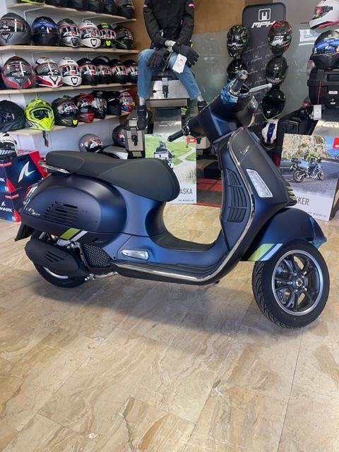 Uno scooter Vespa blu esposto in un negozio, con caschi sullo sfondo.