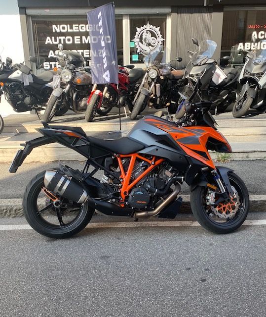 Motocicletta KTM 1290 Super Duke arancione e grigia parcheggiata davanti a un negozio insieme ad altre motociclette.