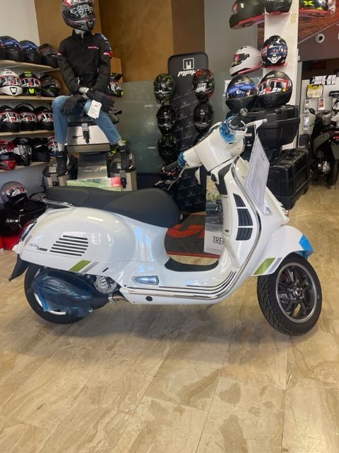 Scooter Vespa bianco in un negozio, con caschi e un manichino sullo sfondo.