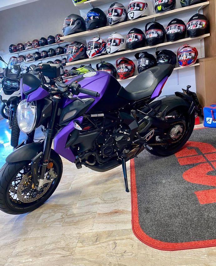 Motocicletta viola e nera in un negozio, con caschi sugli scaffali sullo sfondo.