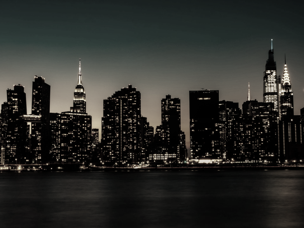 New York City skyline at night with lights reflecting on the water.