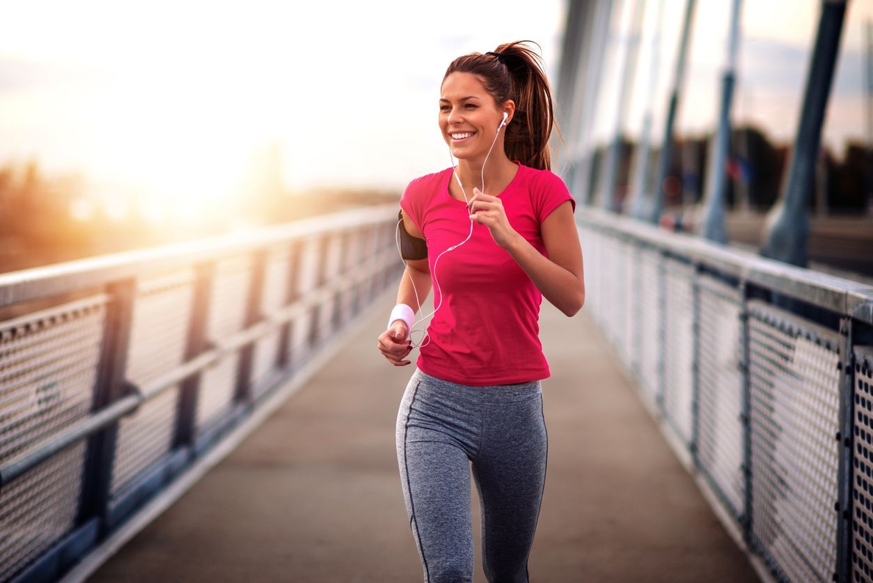 Woman jogging on a bridge at sunrise, wearing a pink shirt and gray leggings.