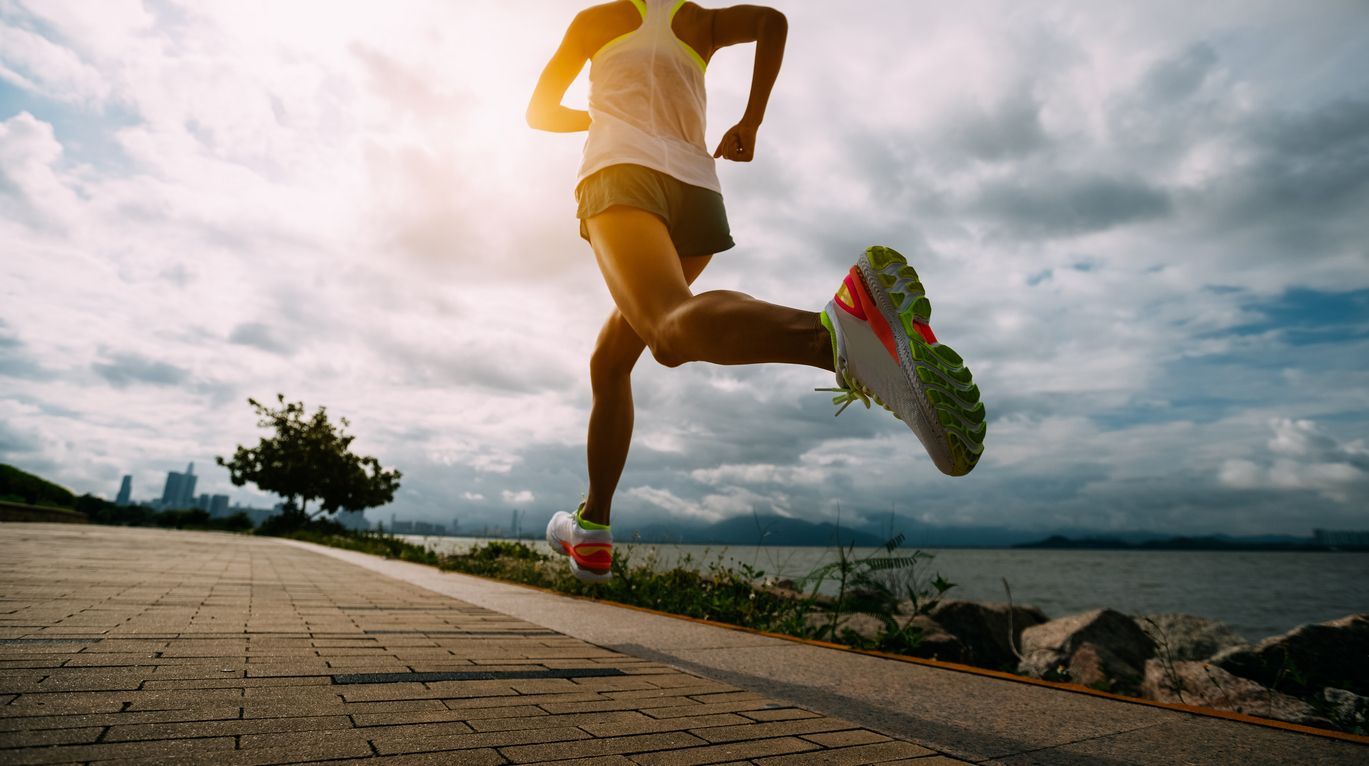 Runner in yellow shirt sprinting on a paved path under a cloudy sky
