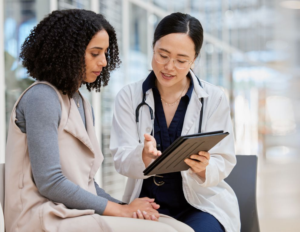 Doctor showing tablet notes to seated patient in a bright clinic waiting area