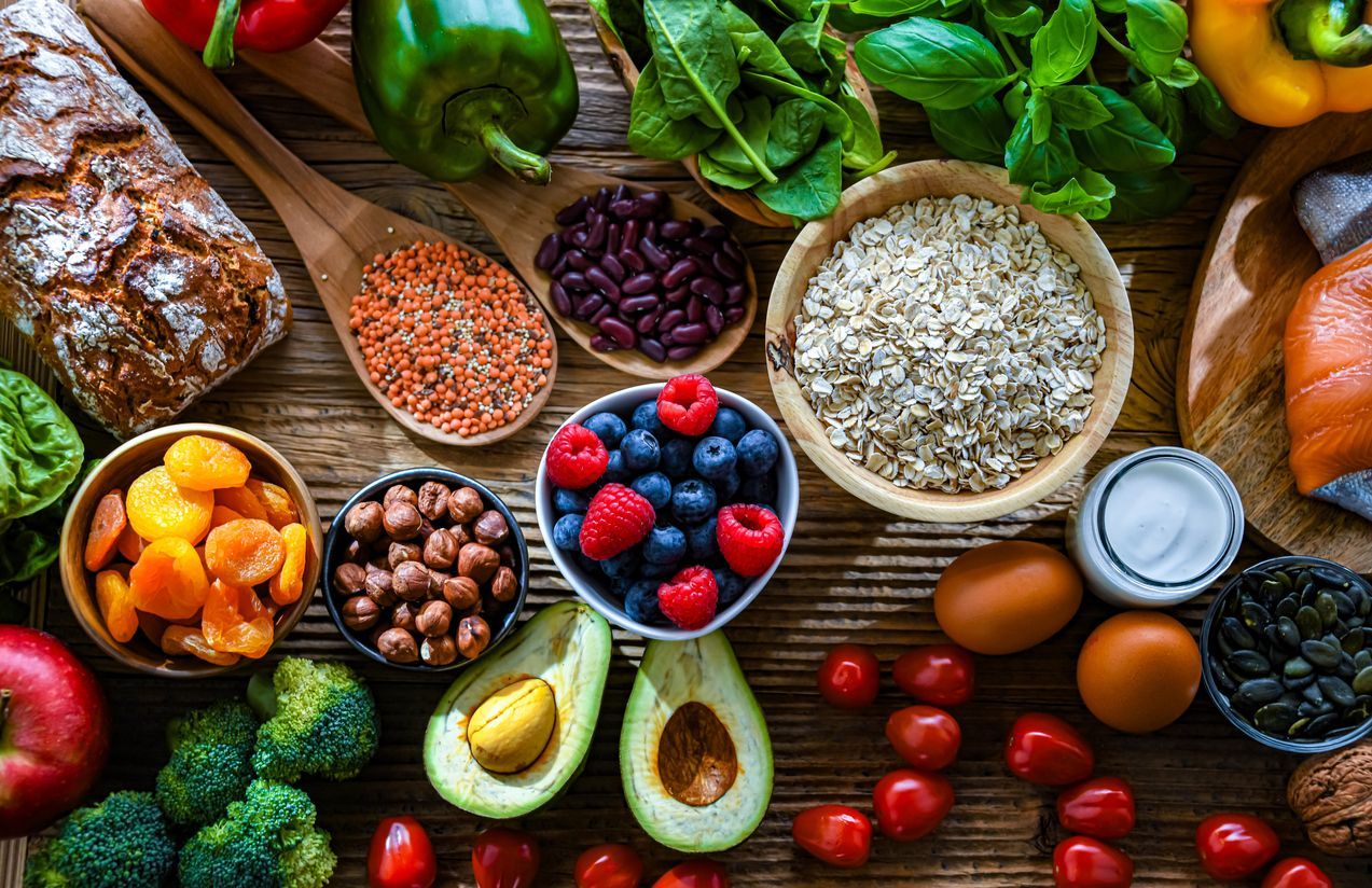 Assorted fresh fruits, vegetables, grains, nuts, and eggs arranged on a rustic wooden table