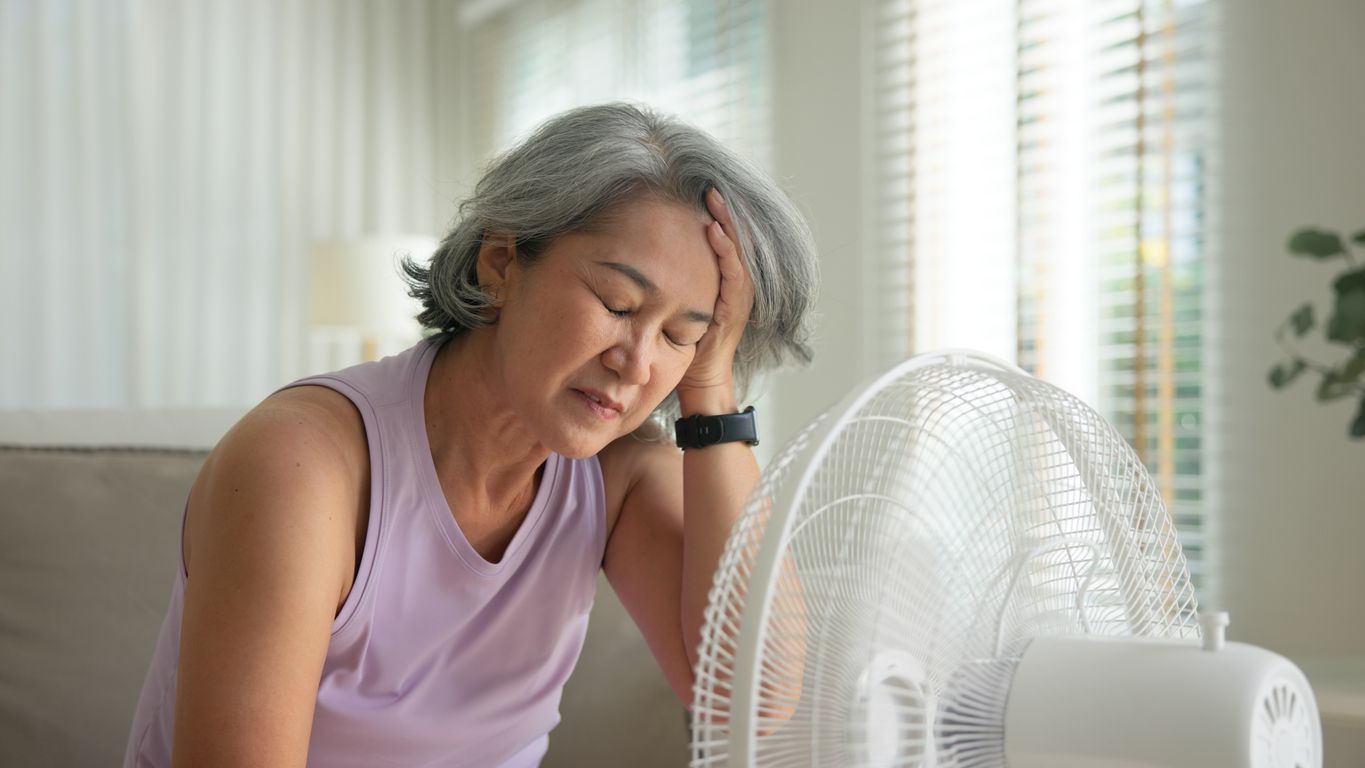 Woman resting beside a white fan indoors on a hot day