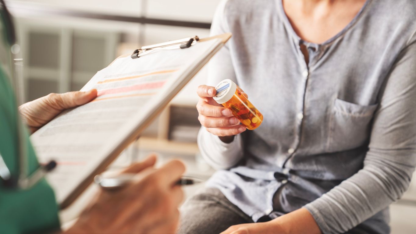 Person holding a prescription bottle while speaking with a doctor holding a clipboard in a clinic