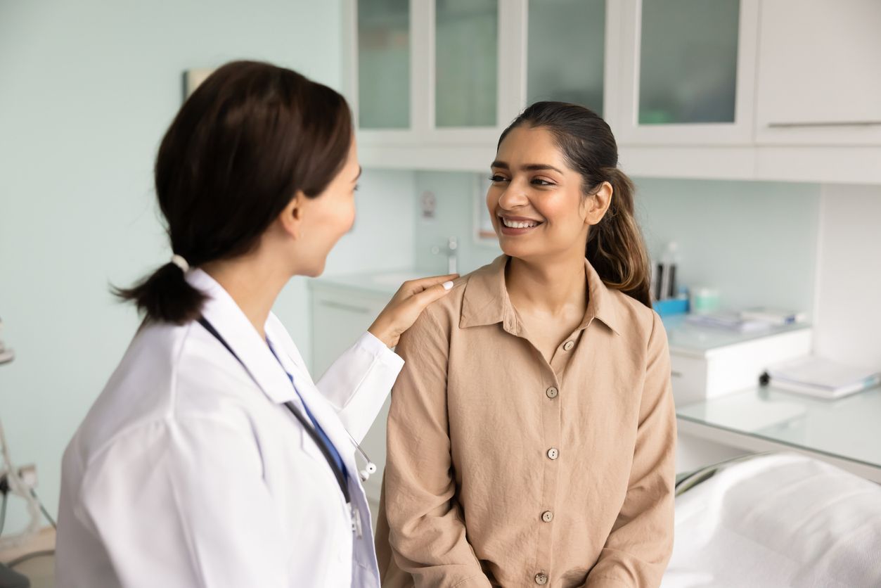 Doctor smiling and talking with a seated patient in a bright clinic room