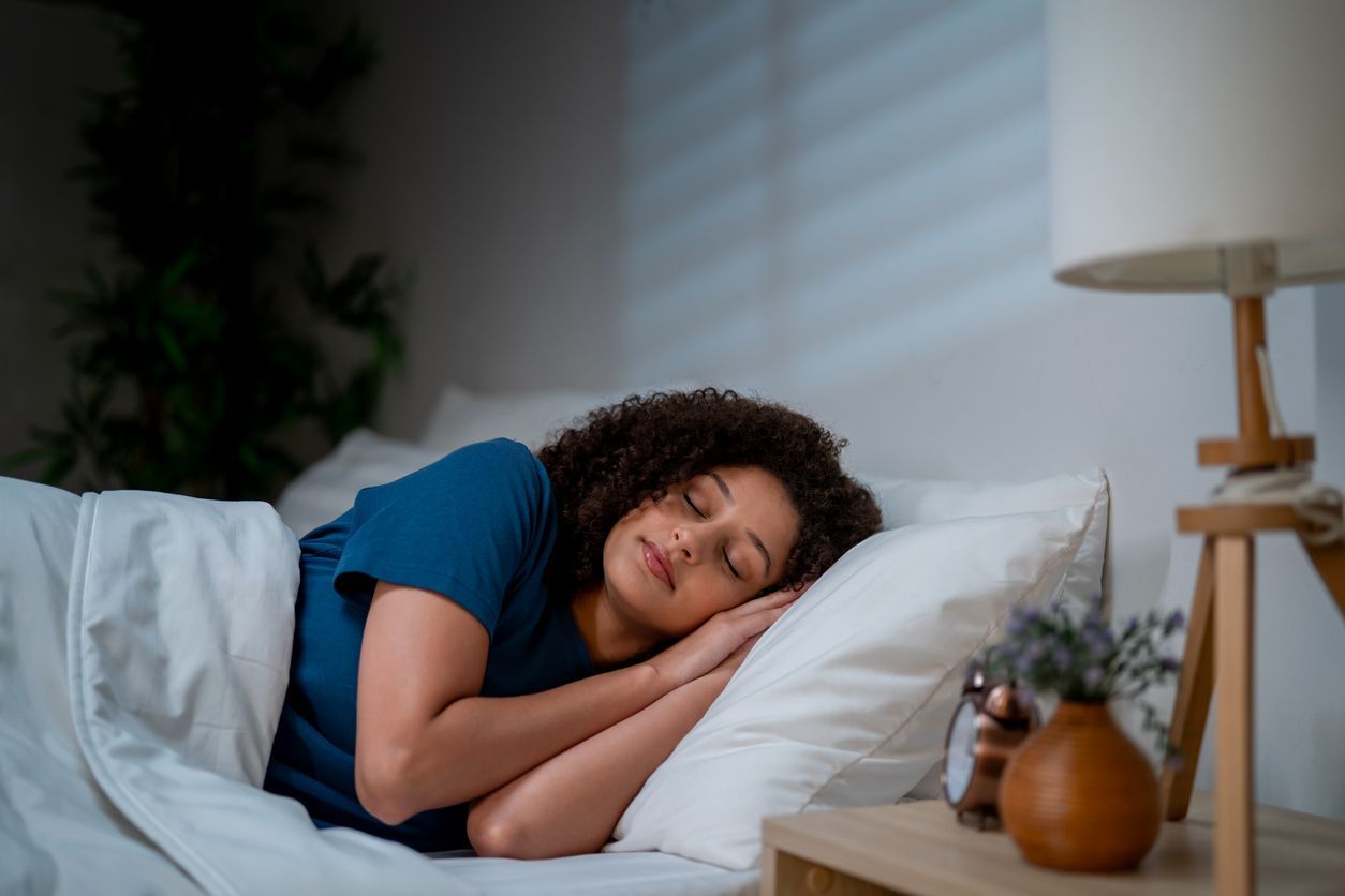 Person sleeping in bed, cuddled under white blankets in a softly lit bedroom.