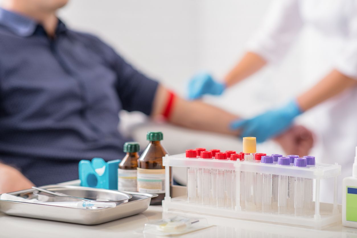 Blood samples in test tubes beside a patient as a clinician draws blood with blue gloves