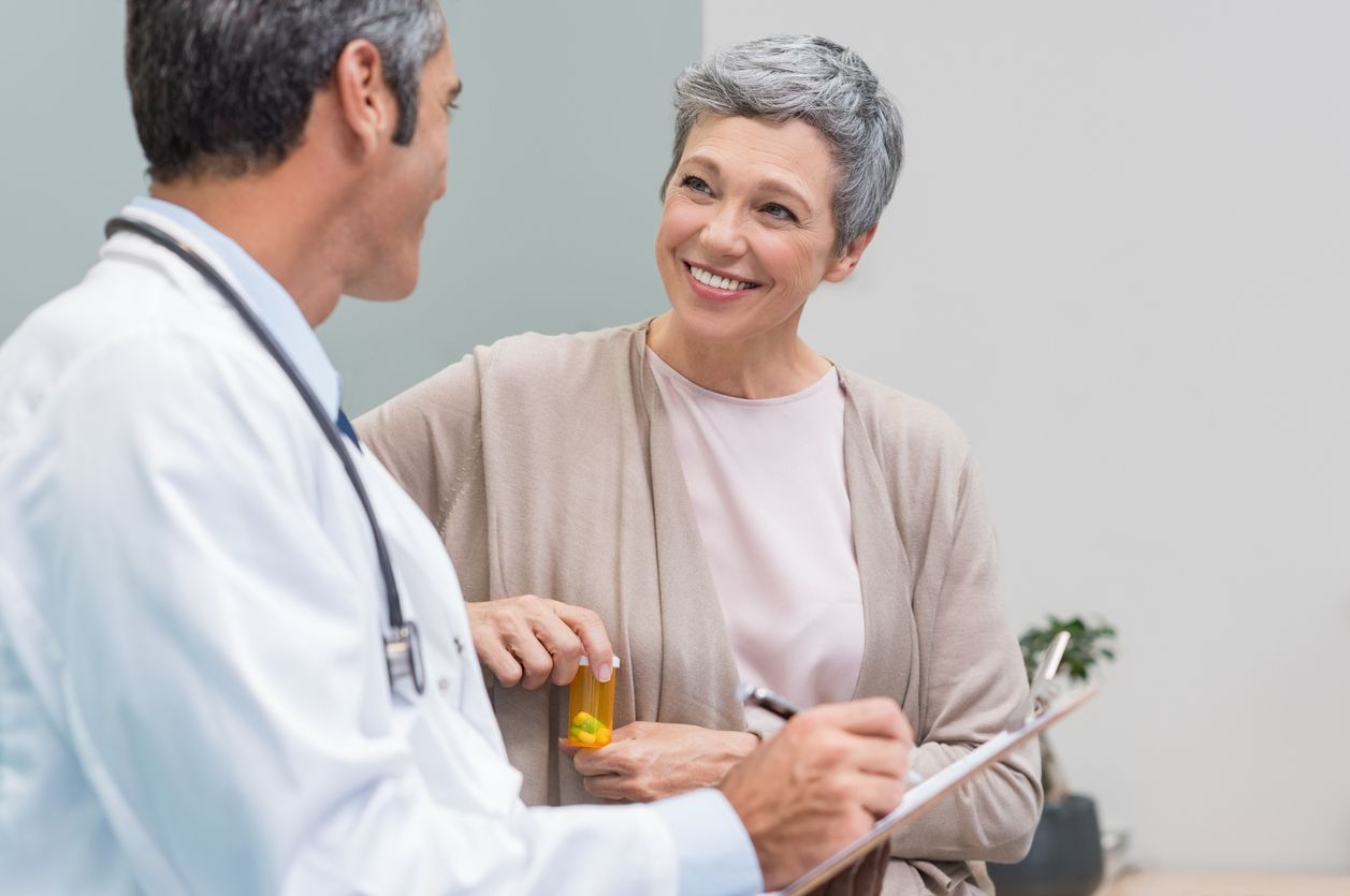 Doctor speaking with a smiling patient holding a pill bottle in a clinic