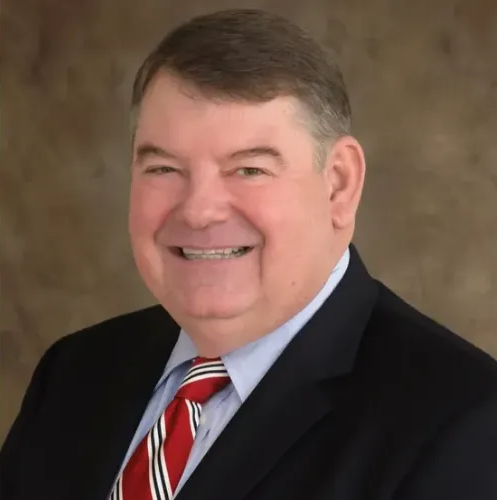 Studio headshot of a smiling man in a dark suit, light blue shirt, and red striped tie