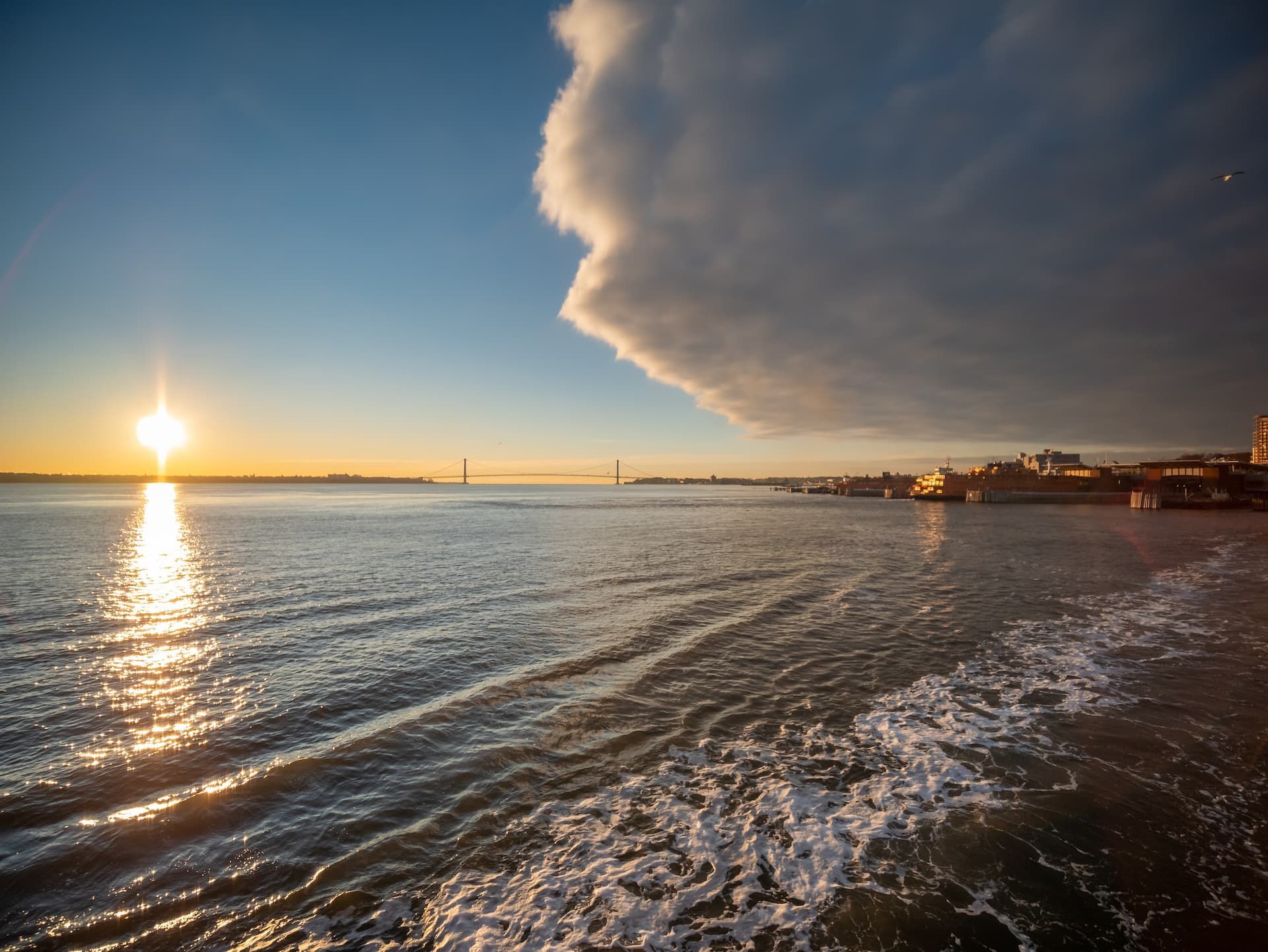 Sunset over calm ocean with rippling water and dramatic clouds above the shoreline