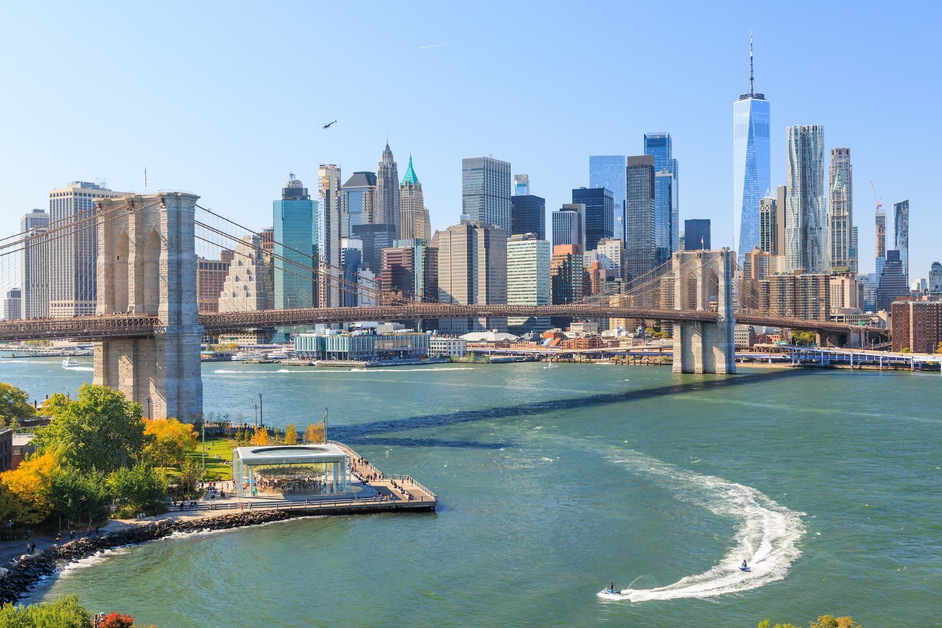 Brooklyn Bridge spanning the East River with Manhattan skyline and One World Trade Center under a blue sky