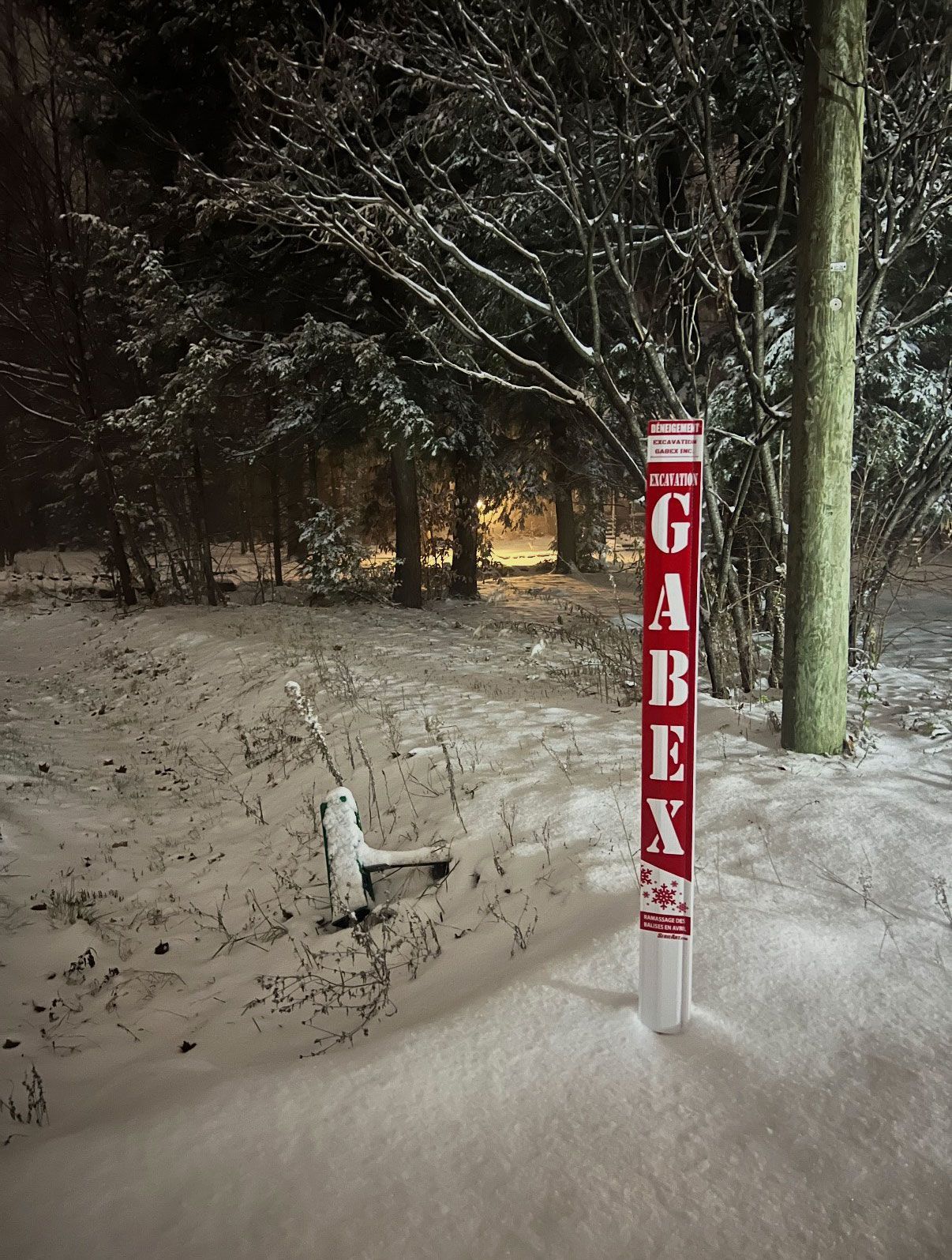 Dans la forêt enneigée, la nuit, un poteau indicateur rouge et blanc portant l'inscription « GABEX » se dresse.