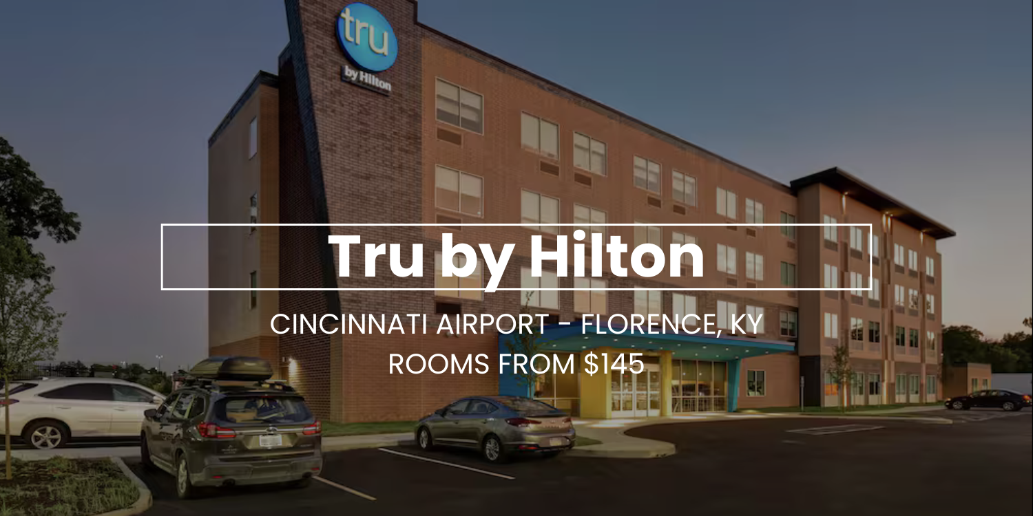 Tru by Hilton Cincinnati Airport Florence hotel exterior at dusk, with parking lot and room rates sign