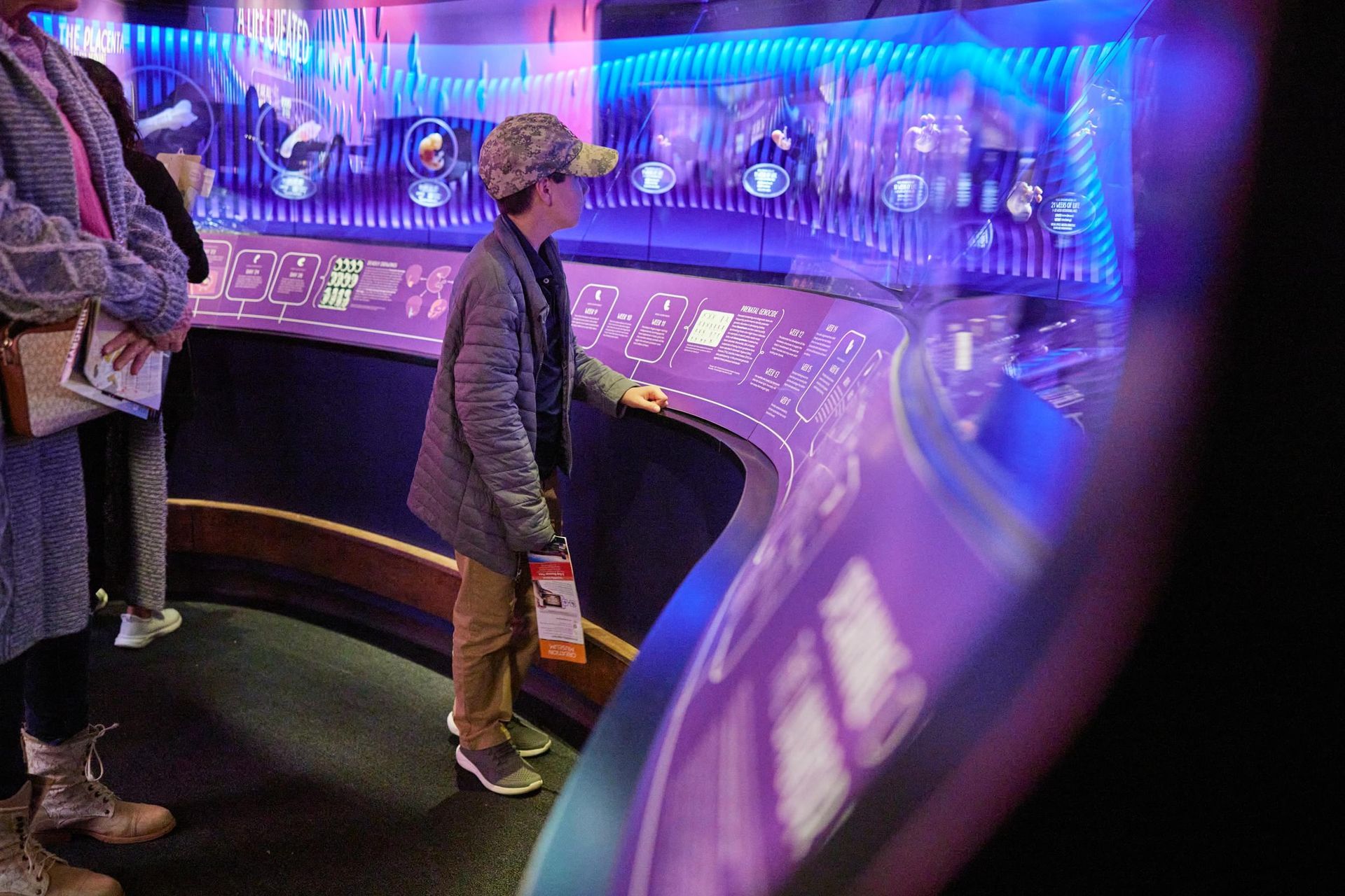 People viewing a glowing blue-purple interactive exhibit with curved screens and control panels