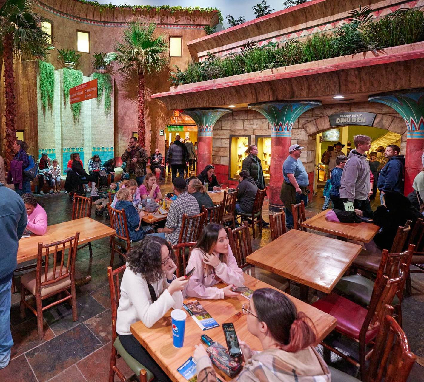 Crowded open-air restaurant with wooden tables, colorful lights, and people dining and socializing