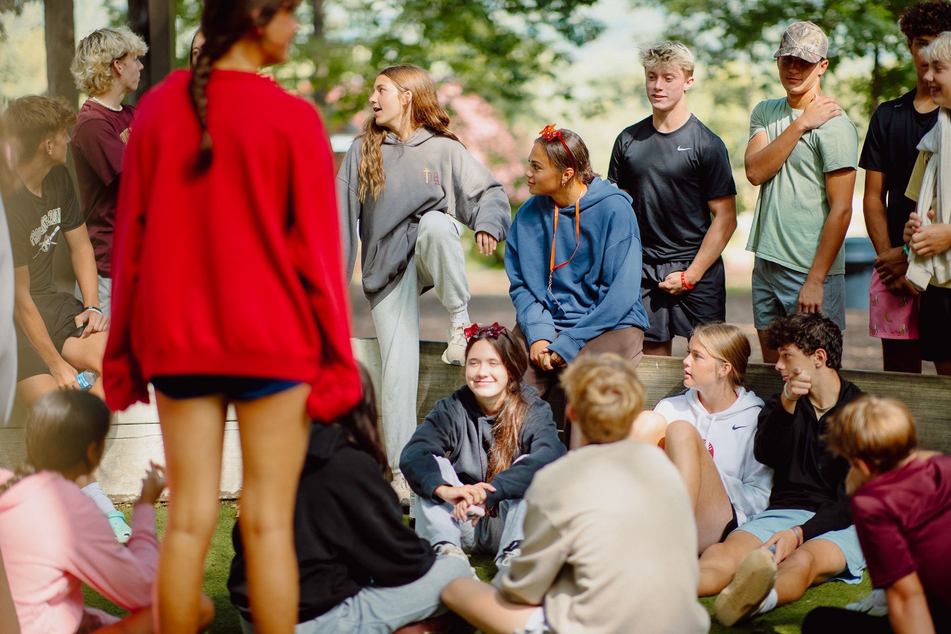 Group of people gathered outdoors in a park, sitting and standing in casual conversation.