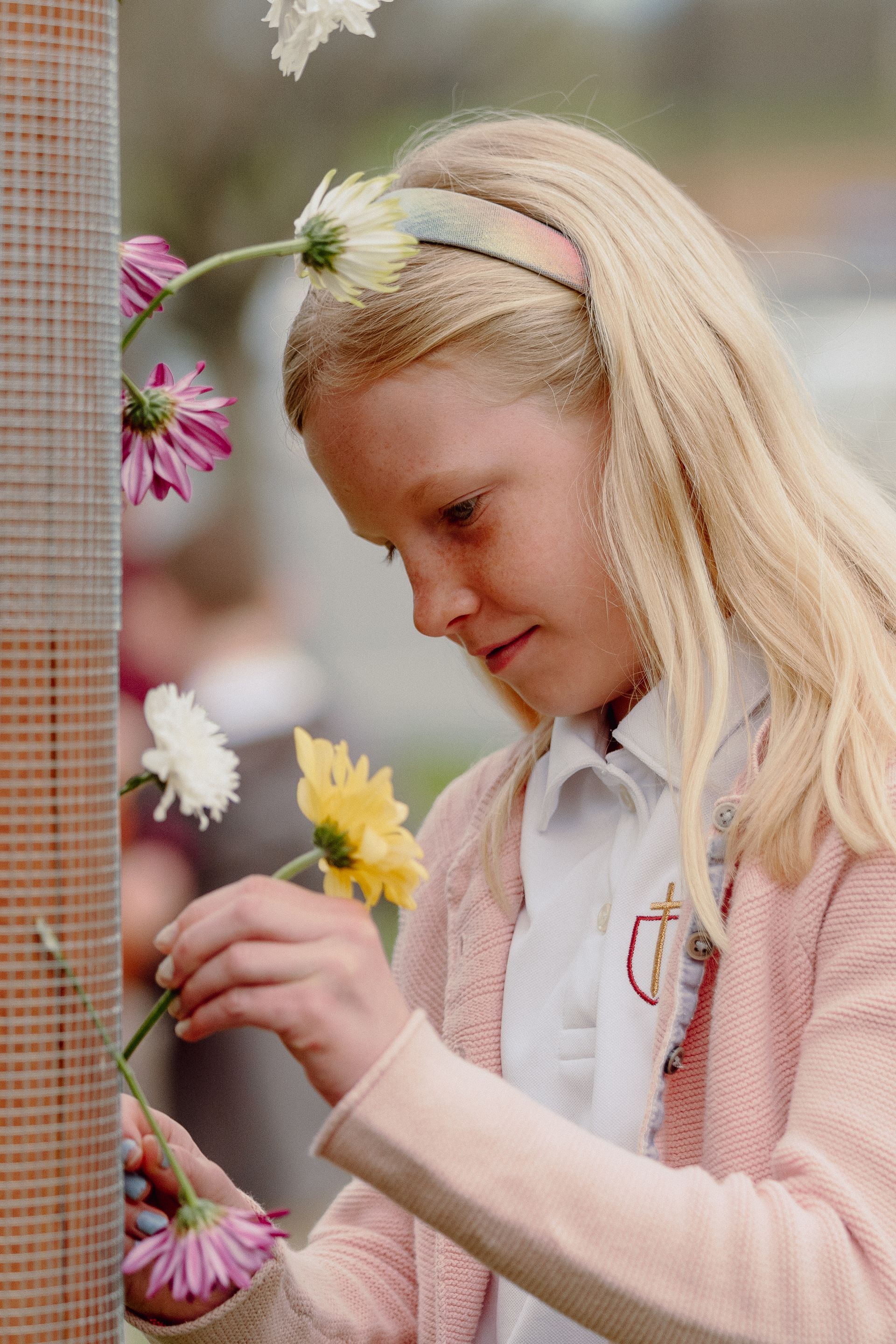 Blonde child arranging colorful flowers on a woven wall display