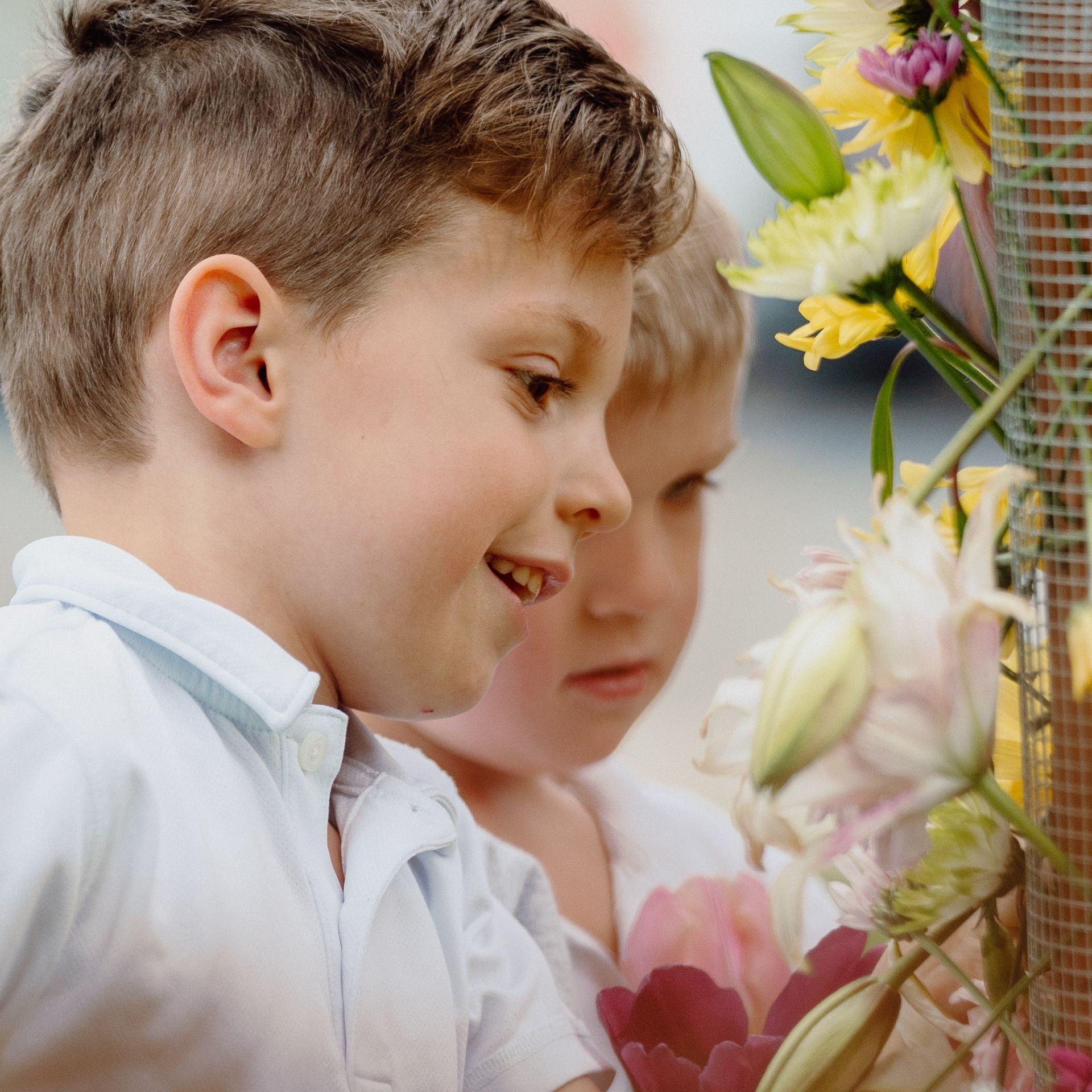 Two children smelling flowers beside a wire fence with colorful blooms