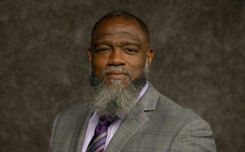 Man in a gray suit and purple tie posing against a brown studio backdrop