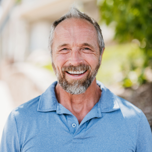 Smiling man in a light blue polo shirt outdoors with a blurred sunny background