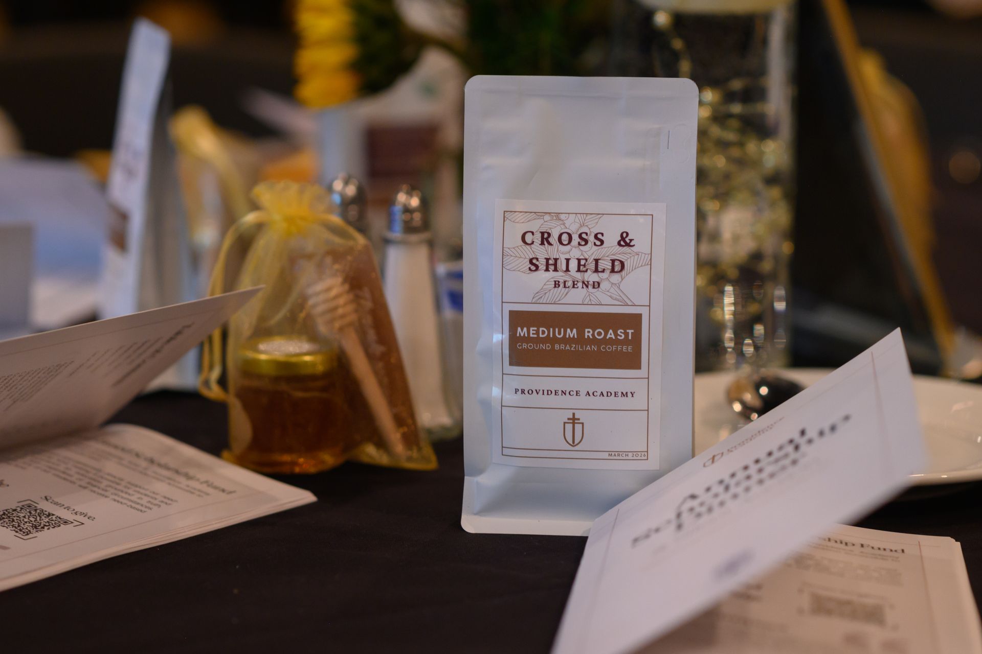 Coffee bags and menu cards on a black table, with a clear glass pitcher in the background