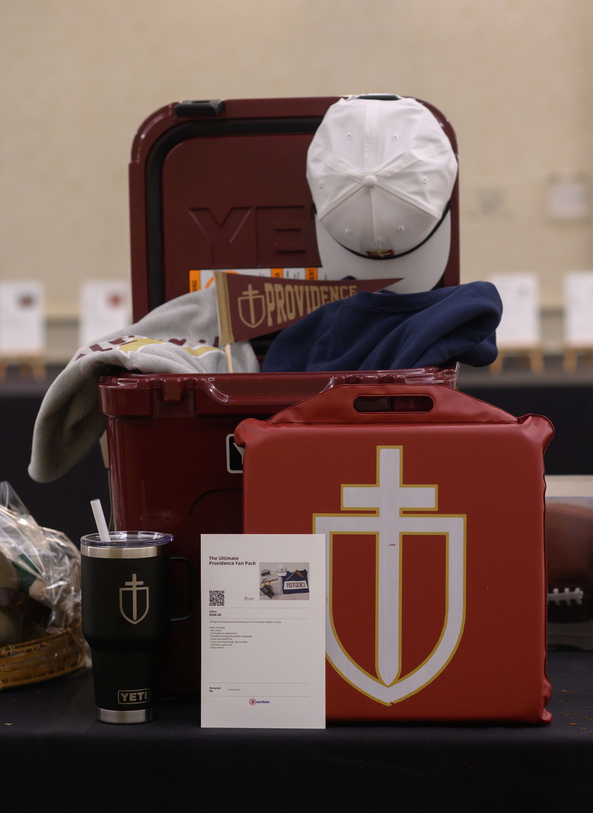 Red cooler with white emblem, white cap, black tumbler, and card on a table indoors