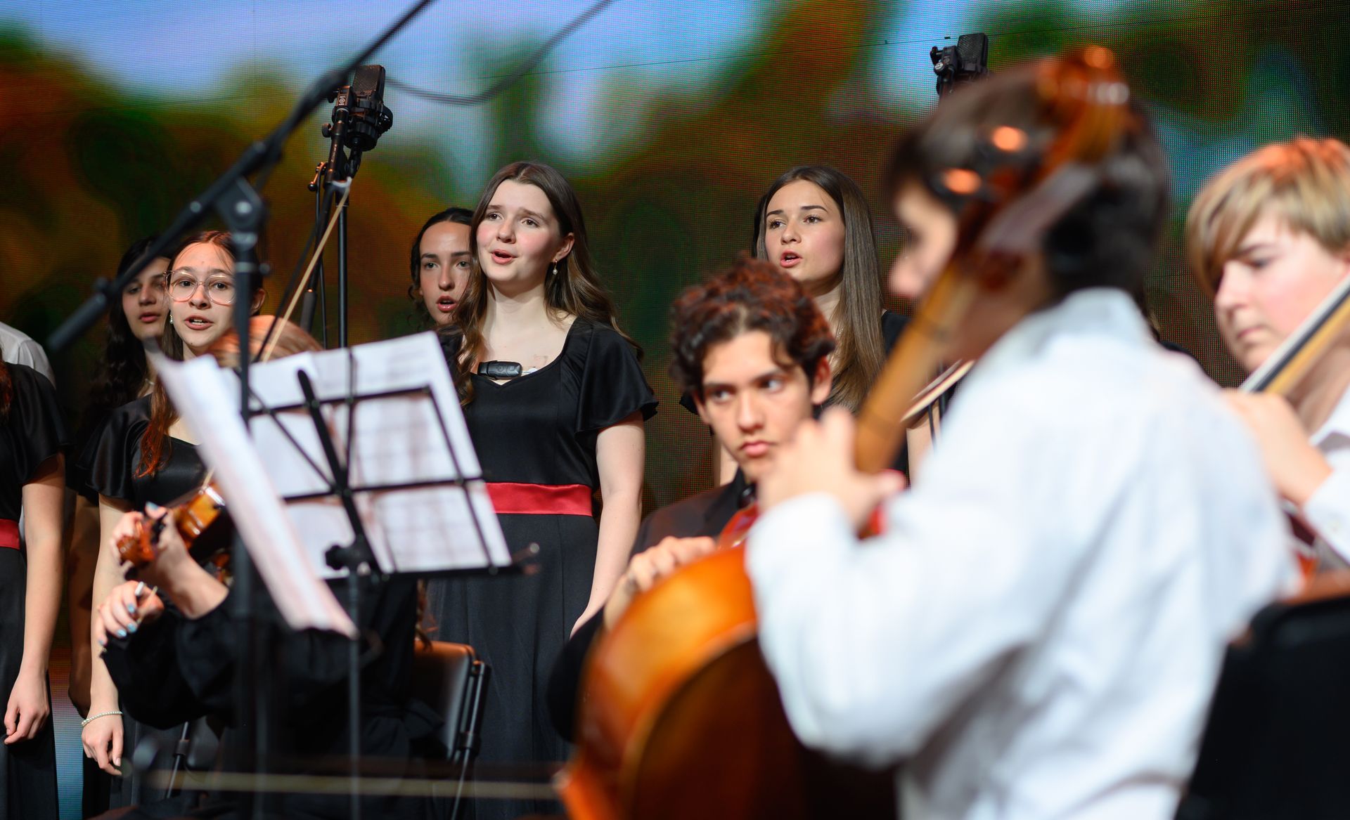 Musicians performing outdoors, with singers and string players around a music stand and microphone