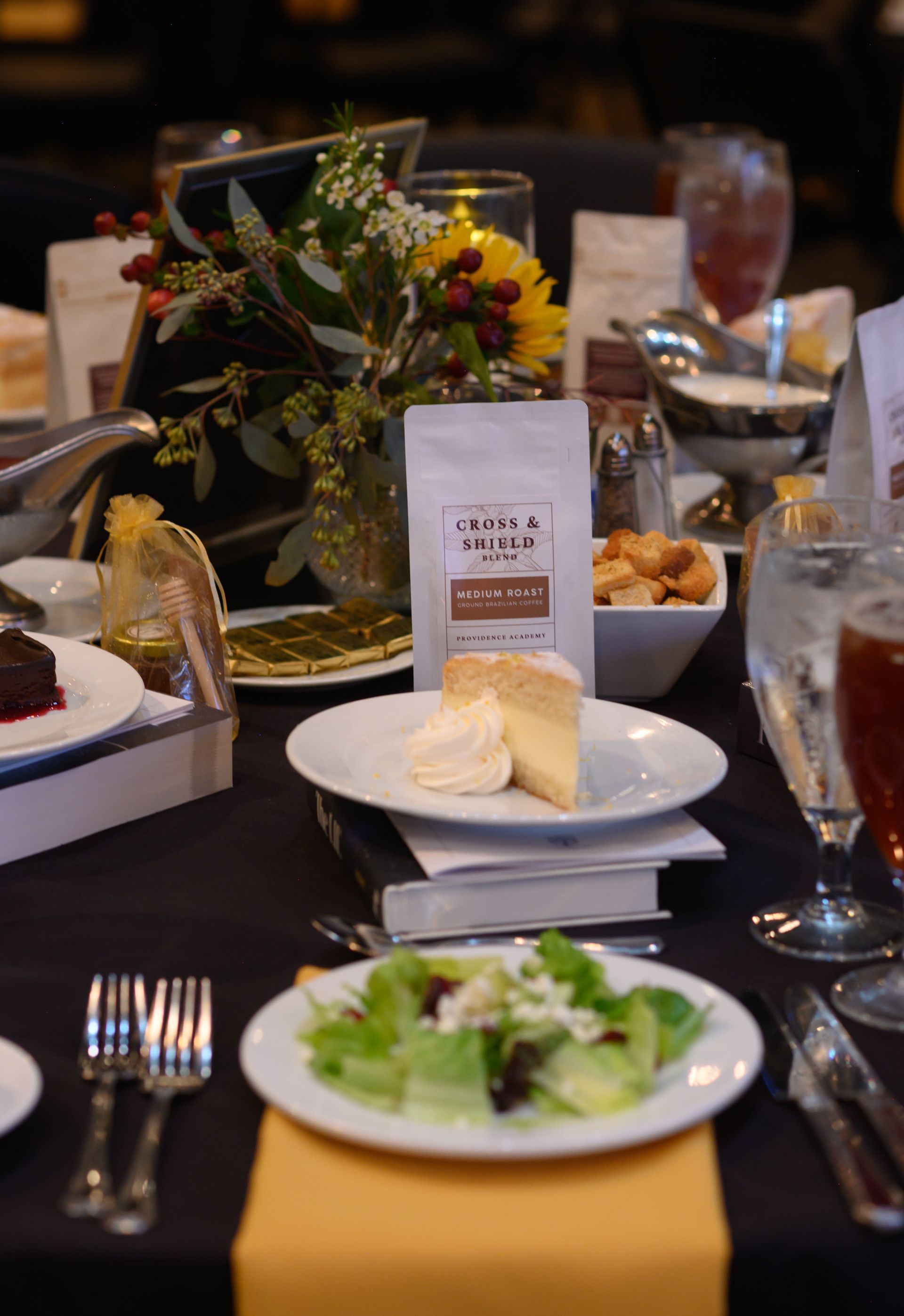 Elegant restaurant table with plated salads, bread, drinks, and a floral centerpiece on a black tablecloth