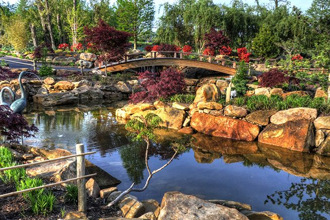 Landscaped garden with a pond, stone bridge, and colorful flowers reflecting in the water