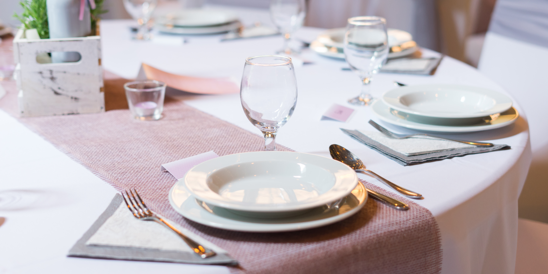 Elegant dining table with white plates, gold cutlery, wine glasses, and a pink runner.