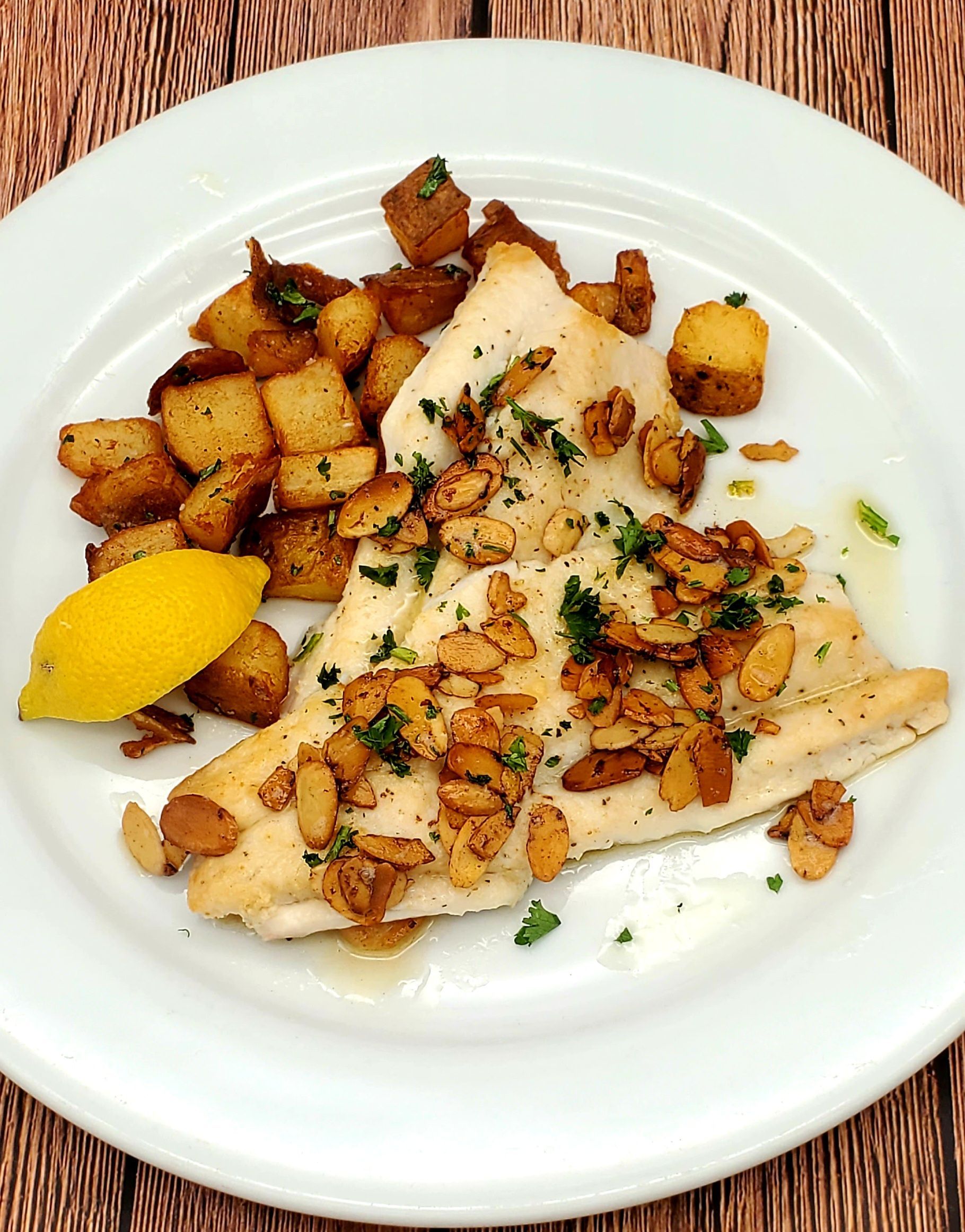 A white plate topped with fish and potatoes on a wooden table.