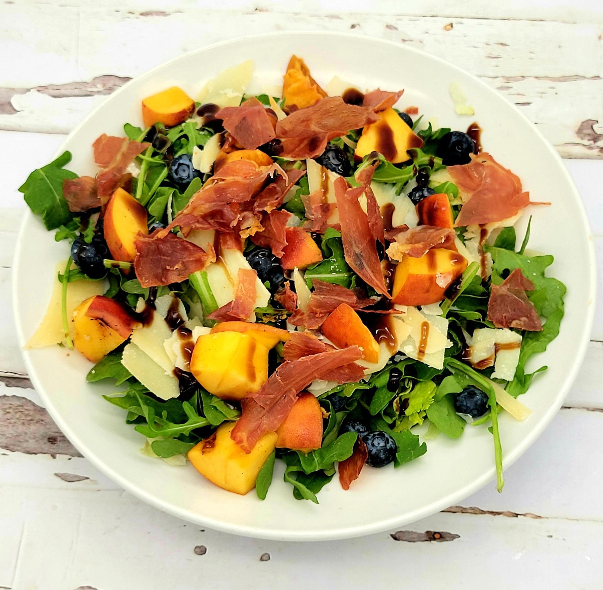 A salad with peaches and blueberries on a white plate