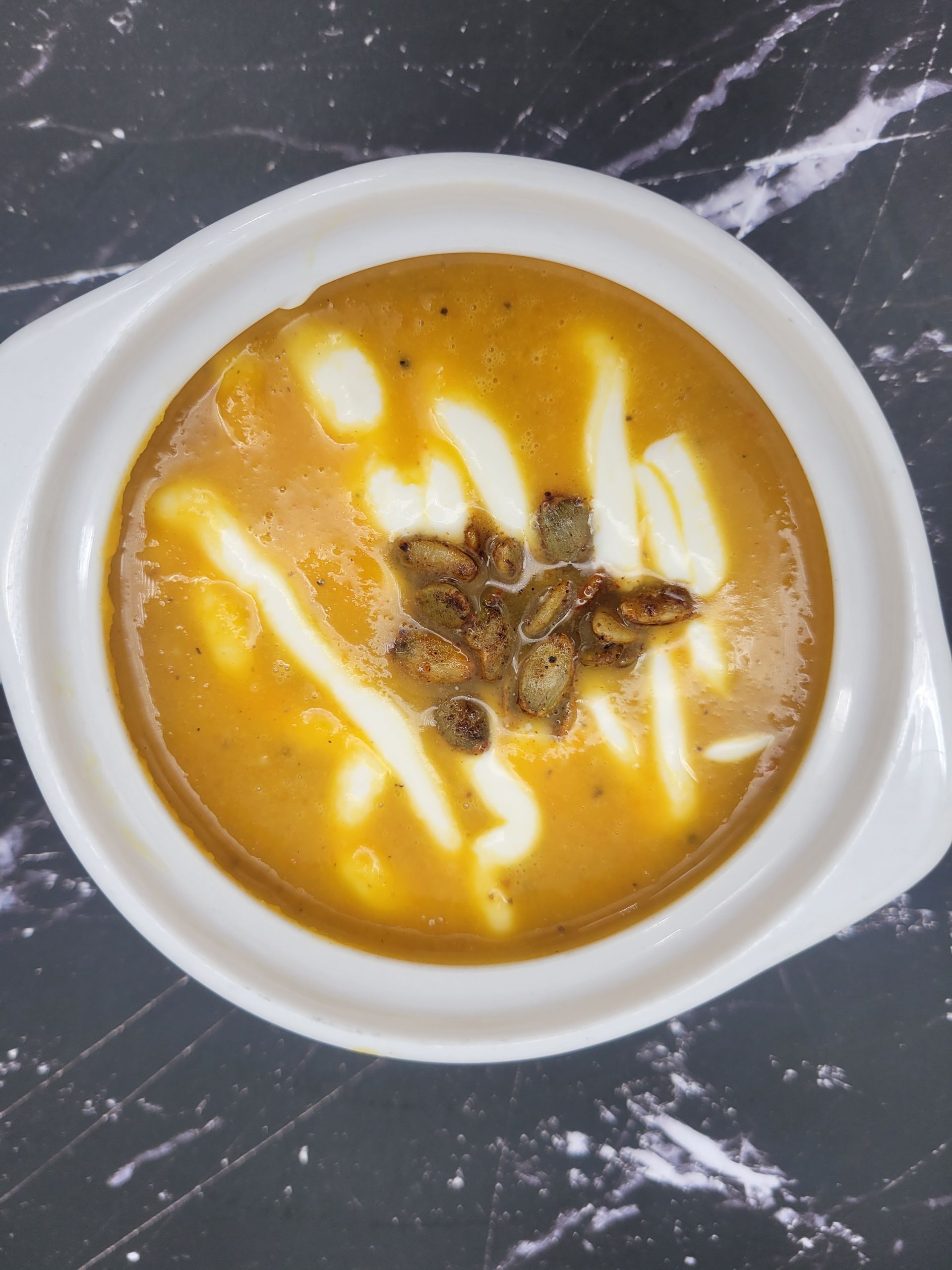 A bowl of soup with cheese and pumpkin seeds on top