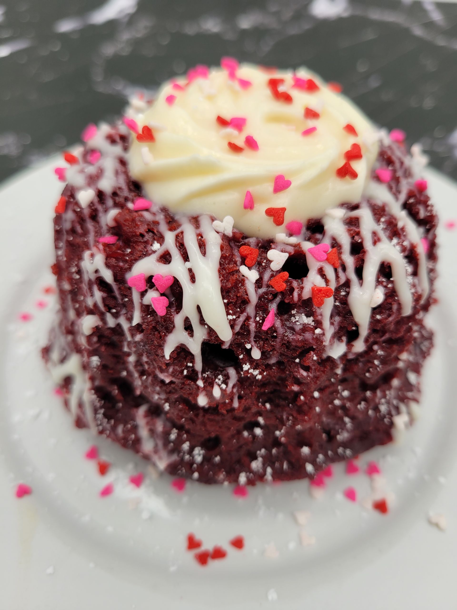 A red velvet cake with white frosting and sprinkles on a white plate