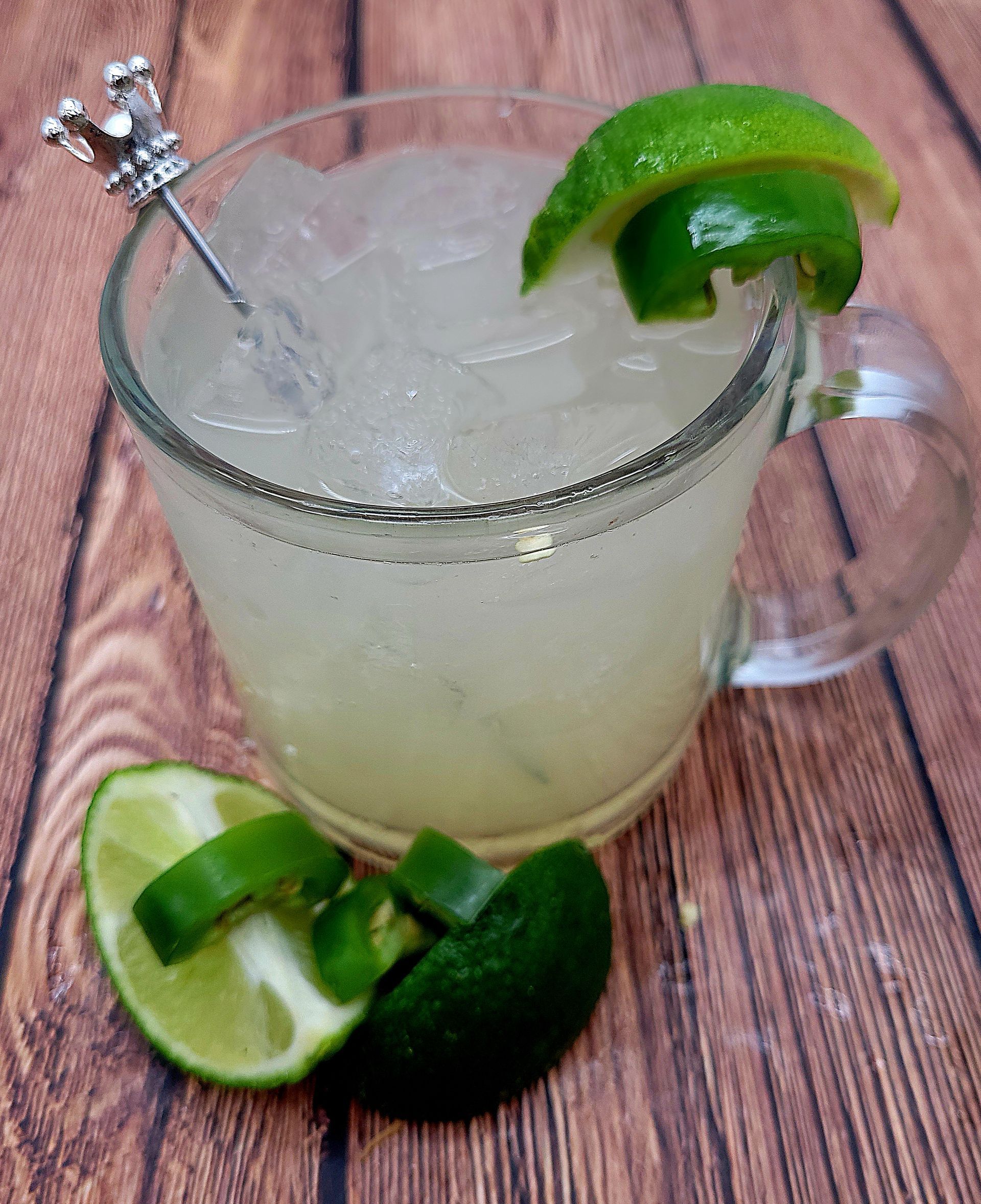 A glass with ice, liquid and lime slices on a wooden table.