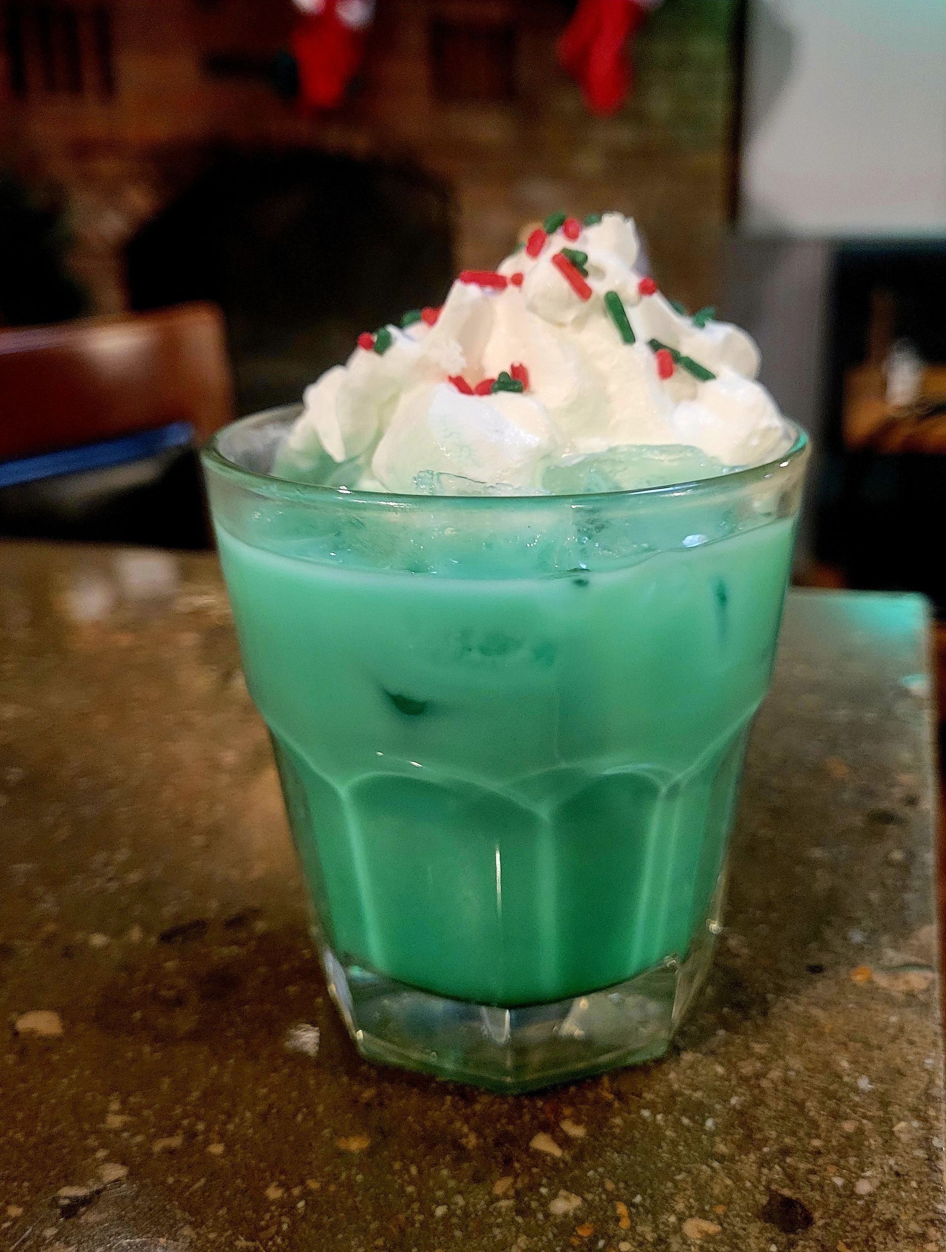 A blue-green drink with whipped cream and sprinkles on top
