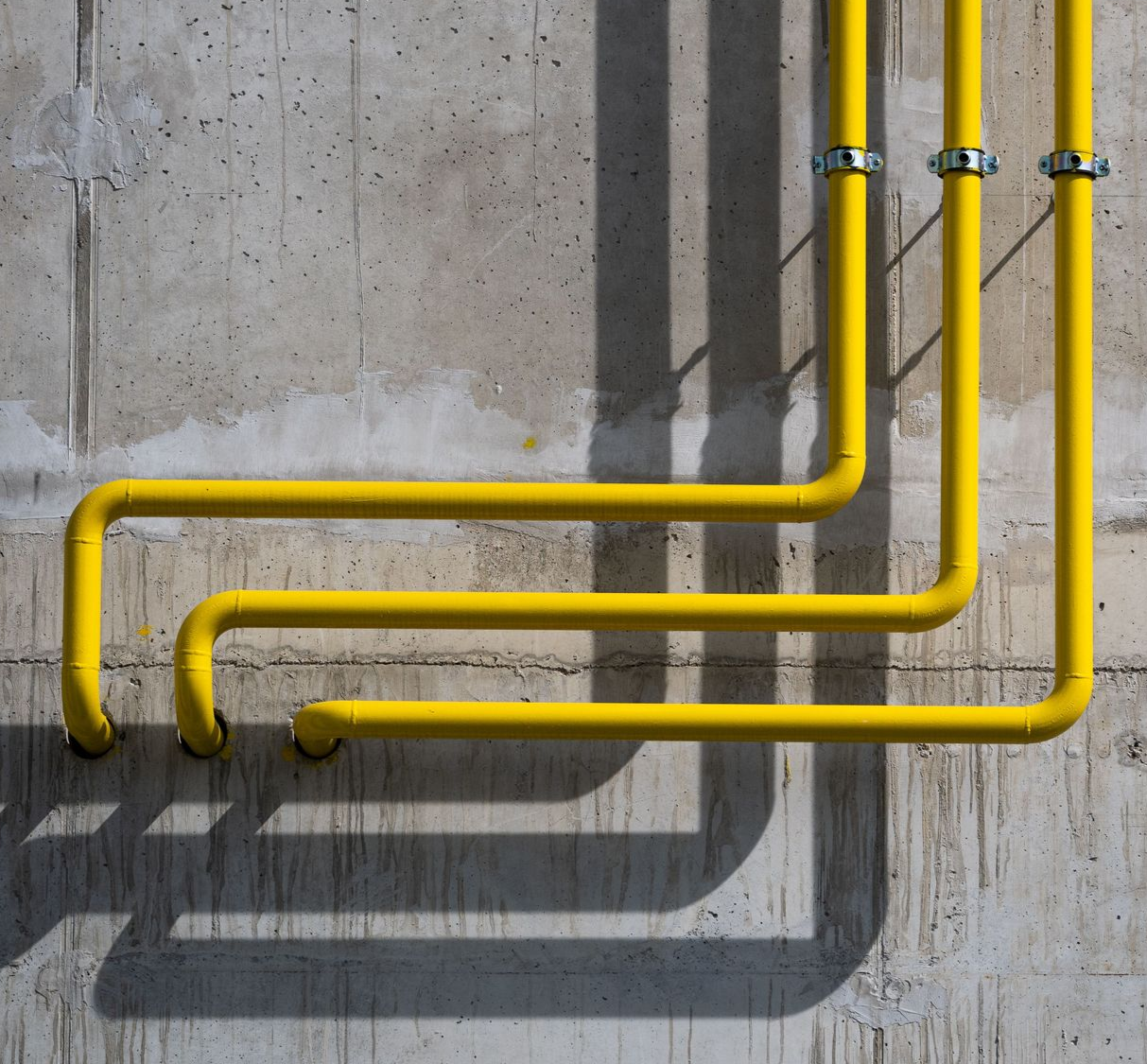 Yellow pipes running along a gray concrete wall, casting long shadows