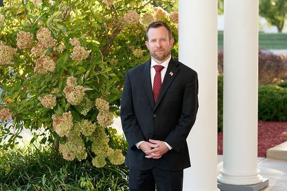 a man in a suit and tie is standing next to a white pillar .