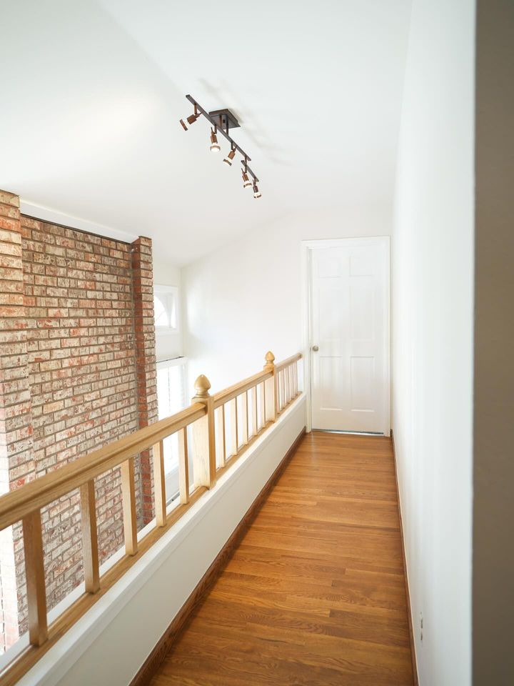 Narrow hallway with exposed brick wall, white door, wood floor, and ceiling light fixture
