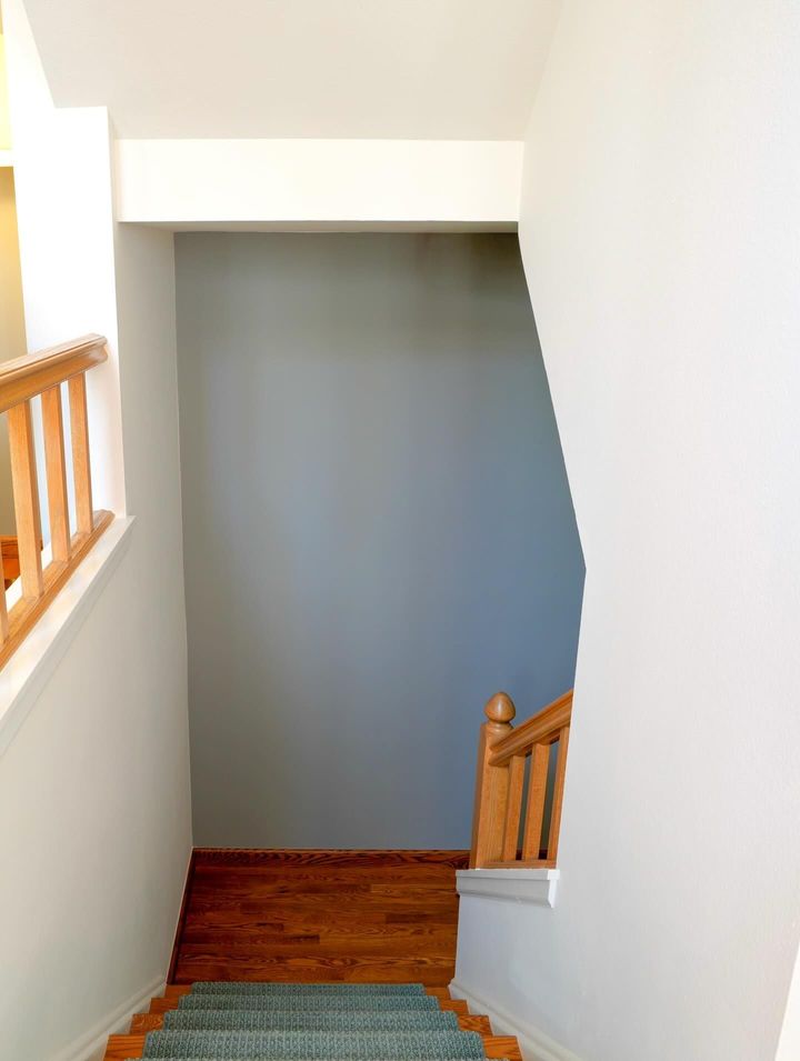 Stairwell with white walls, wood handrails, and a gray landing at the bottom.