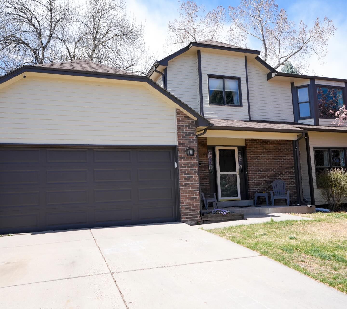 Two-story house with beige siding, brick accents, a dark garage door, and a concrete driveway