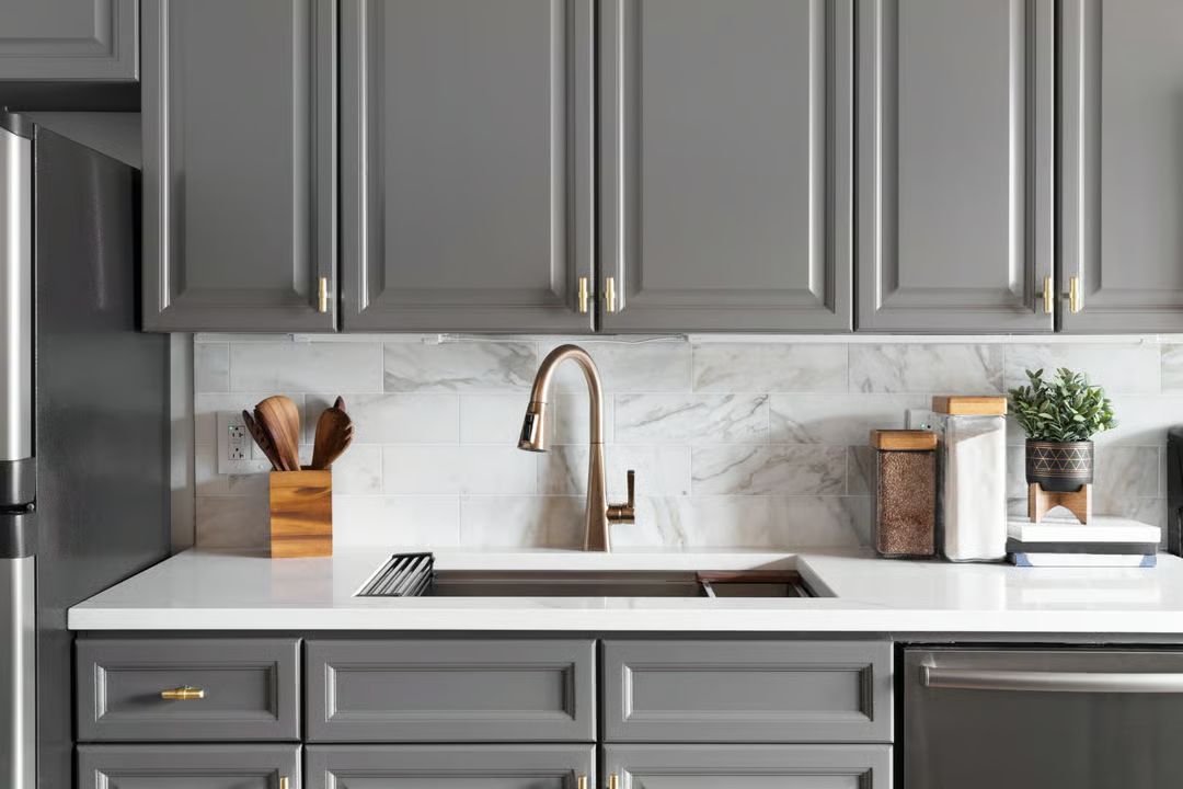 Modern kitchen with gray cabinets, white marble backsplash, and wood-accent decor