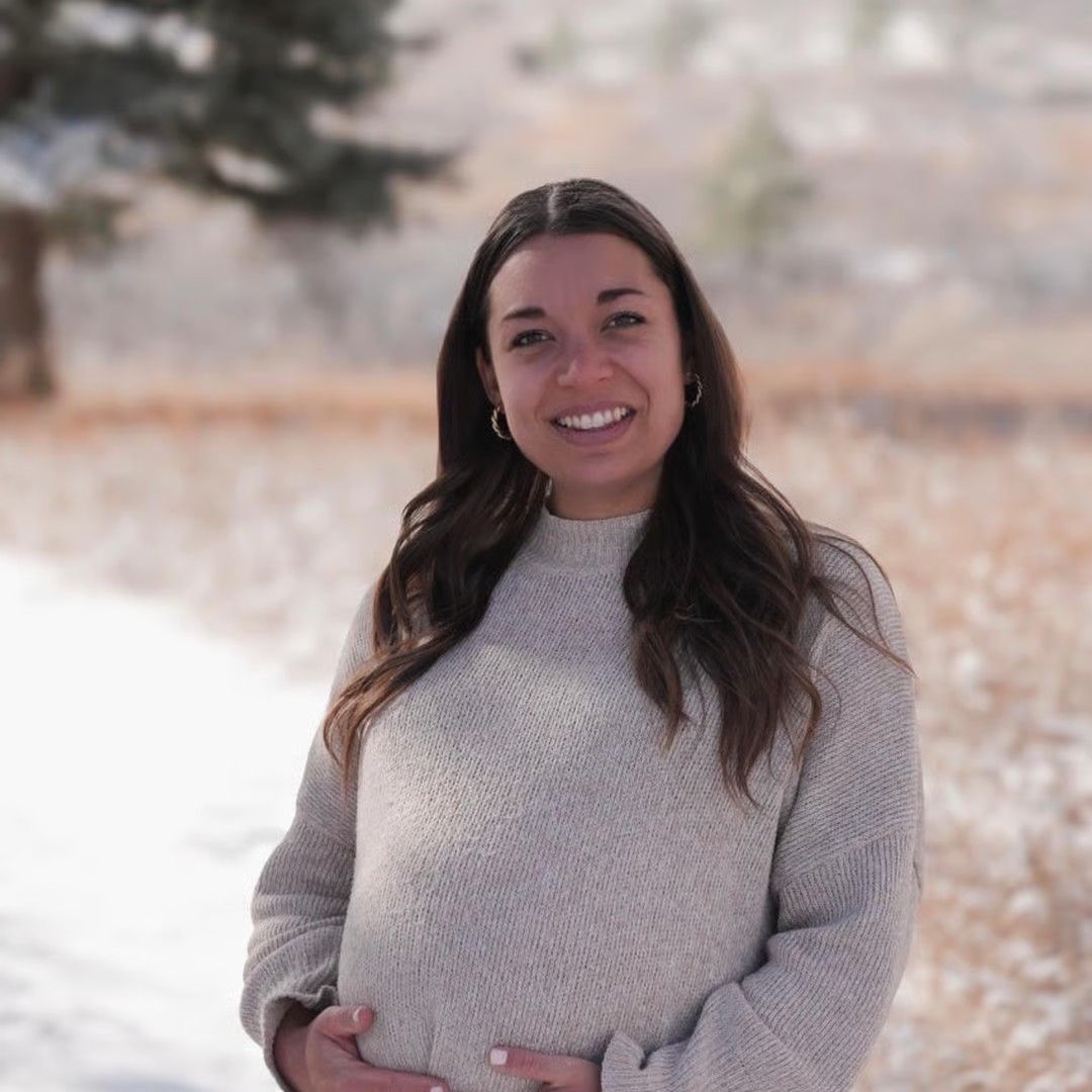 Smiling person in a light sweater standing outdoors in a snowy landscape.