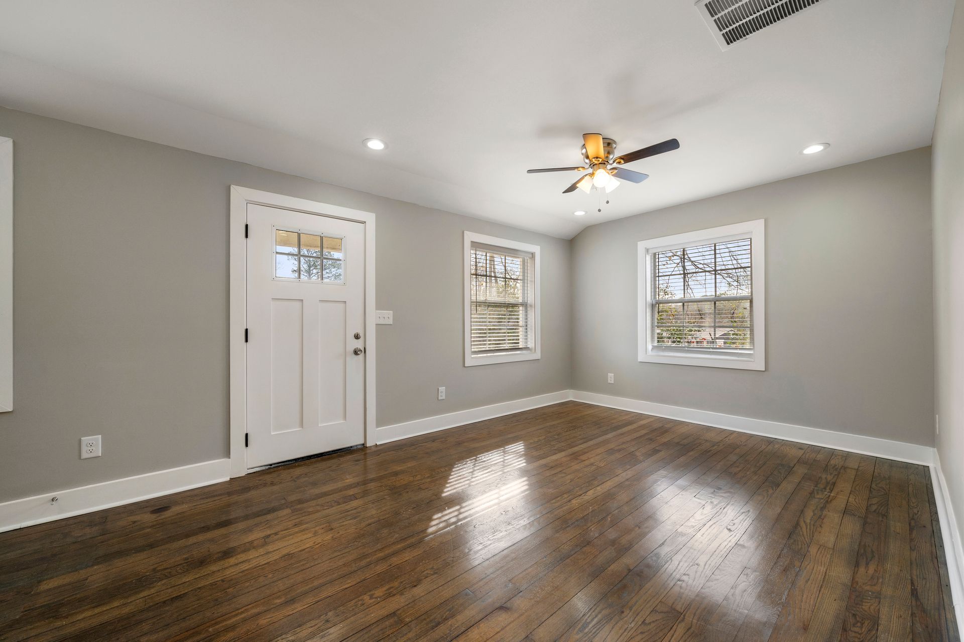 Empty room with dark wood floors, gray walls, white trim, and two windows under a ceiling fan.
