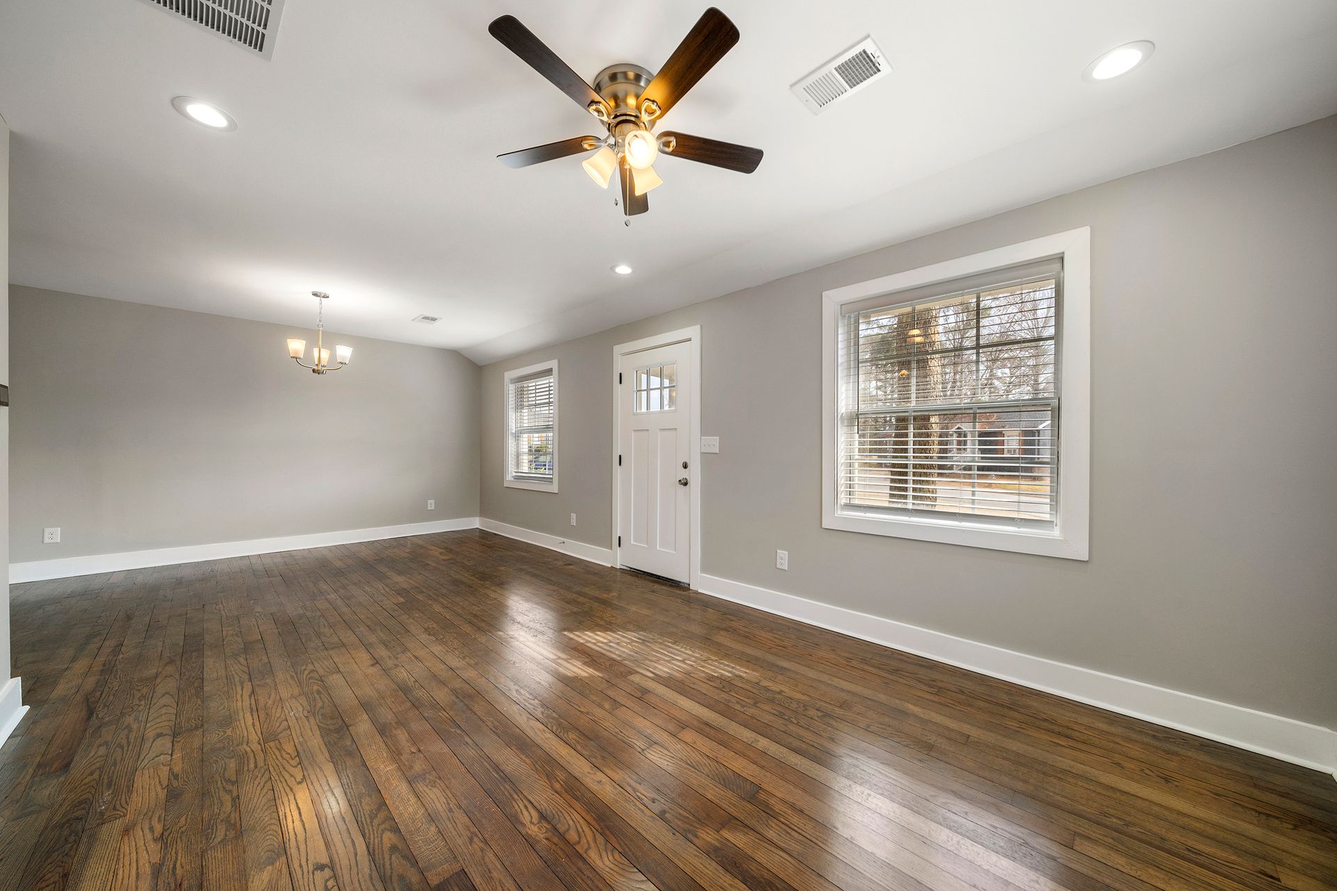 Empty living room with dark wood floors, gray walls, white trim, and ceiling fan under recessed lights