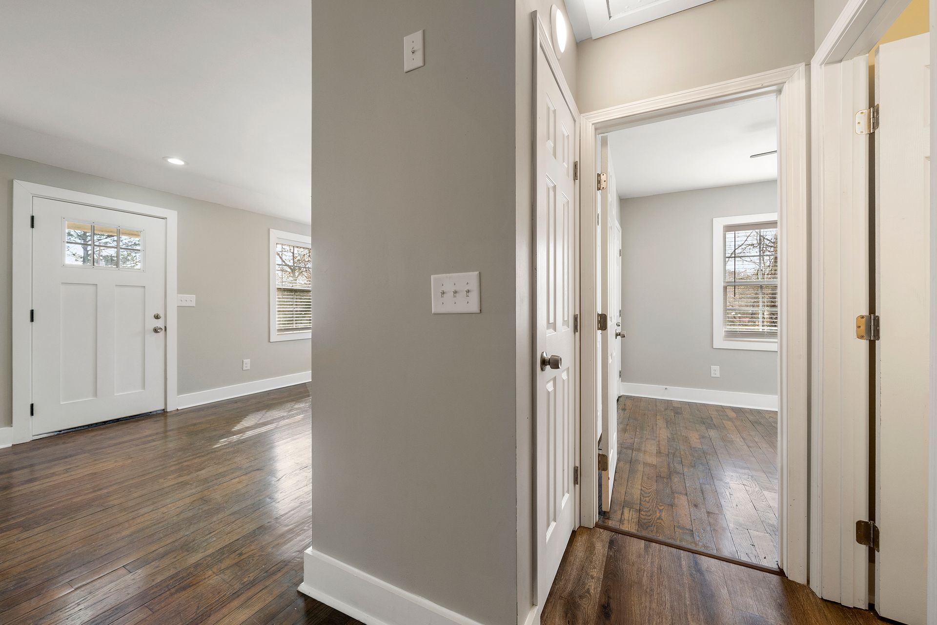 Bright hallway with hardwood floors, white doors, and a front entry with sidelights in a modern home